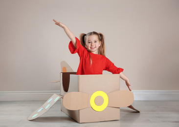 Photo of Cute little child playing with cardboard plane near beige wall
