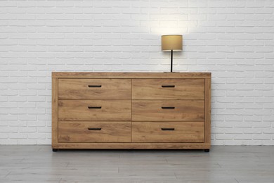Photo of Wooden chest of drawers and lamp near white brick wall. Interior design