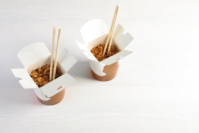 Chinese noodles in paper box on white wooden table, space for text. Food delivery