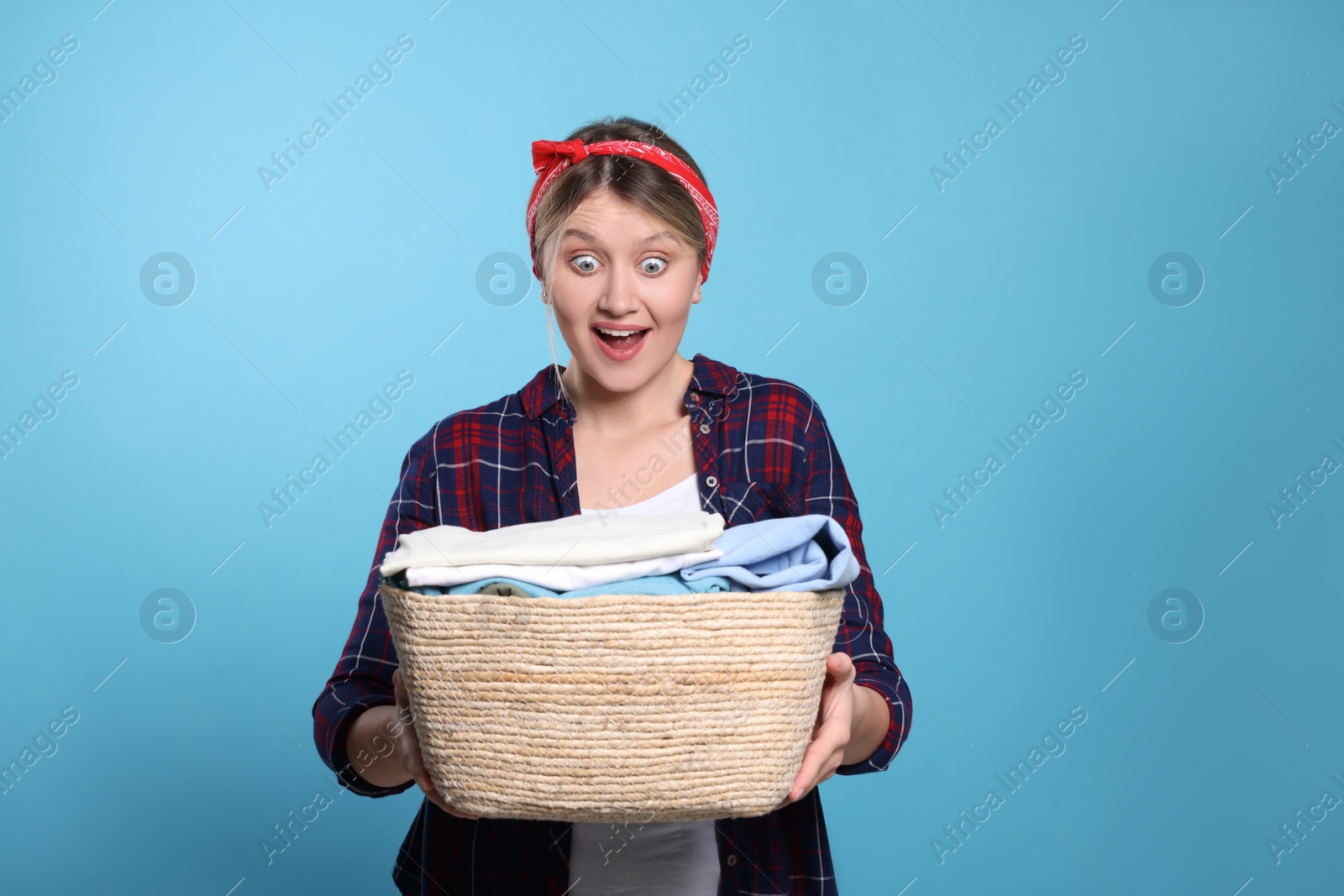 Photo of Emotional woman with basket full of laundry on light blue background