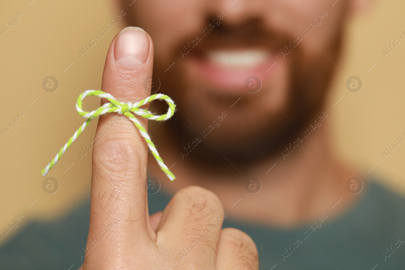 Photo of Man showing index finger with tied bow as reminder against beige background, focus on hand