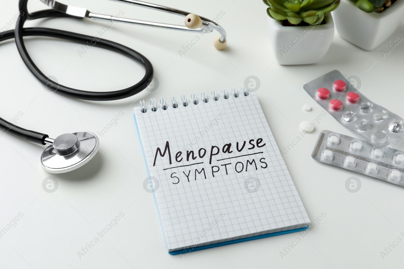 Photo of Notebook with words Menopause Symptoms, pills and stethoscope on white table