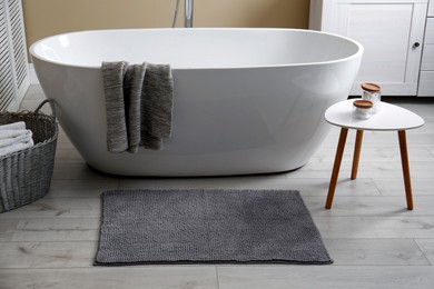 Photo of Soft grey mat on floor near tub in bathroom. Interior design