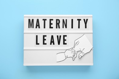 Lightbox with words Maternity Leave and paper cutout of hands on light blue background, top view