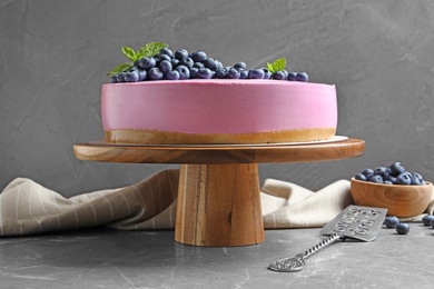 Wooden stand with tasty blueberry cake on grey table