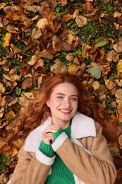 Smiling woman lying among autumn leaves outdoors, top view