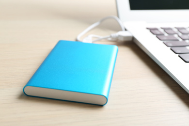 Photo of Charging modern laptop with power bank on wooden table, closeup