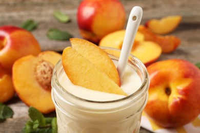 Tasty peach yogurt with pieces of fruit and spoon in glass jar on table, closeup