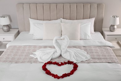 Photo of Beautiful composition on bed. Swans made of towels and rose petals arranged in heart shape