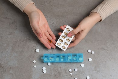 Photo of Woman taking pills from plastic box at grey table, top view