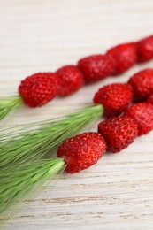 Photo of Grass stems with wild strawberries on white wooden table, closeup