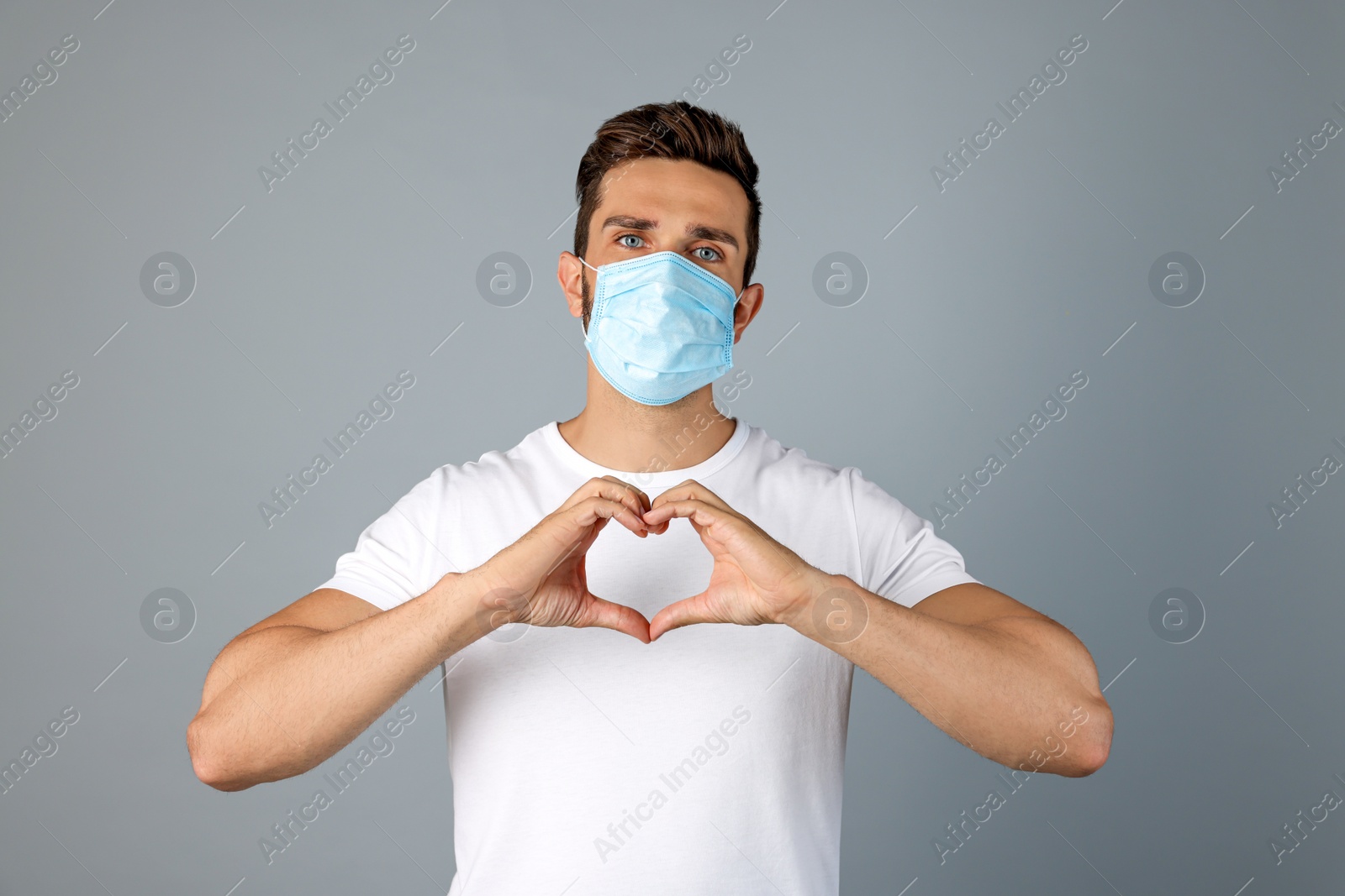 Photo of Man in protective mask making heart with hands on grey background