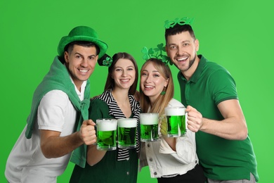 Happy people in St. Patrick's Day outfits with beer on green background