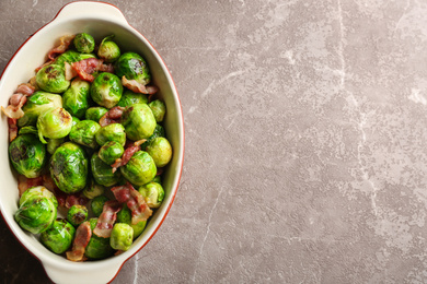 Photo of Delicious Brussels sprouts with bacon on marble table, top view. Space for text