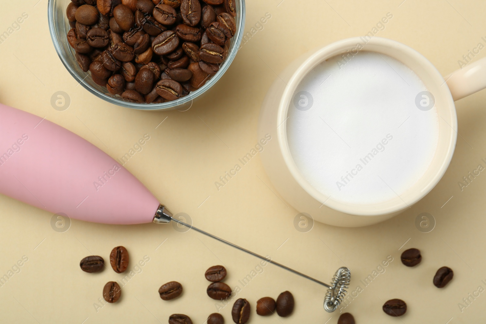 Photo of Mini mixer (milk frother), cup of whipped milk and coffee beans on beige background, flat lay