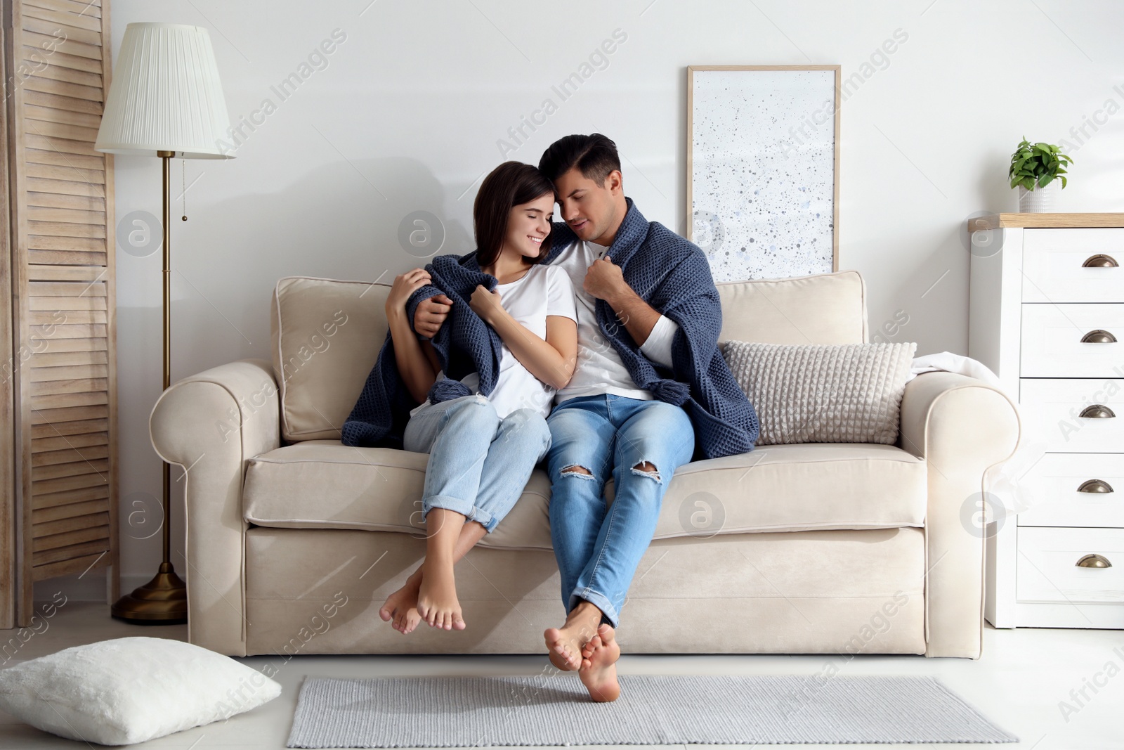 Photo of Happy couple in love covered with warm dark blue plaid sitting on sofa at home