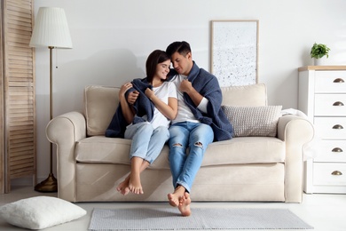 Happy couple in love covered with warm dark blue plaid sitting on sofa at home