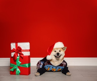 Photo of Cute Akita Inu dog in Christmas sweater and Santa hat near gift boxes indoors
