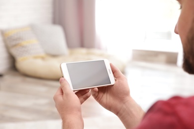 Young man using video chat on smartphone at home, closeup. Space for design