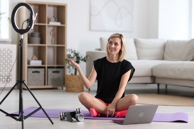 Smiling sports blogger streaming online fitness lesson with smartphone at home