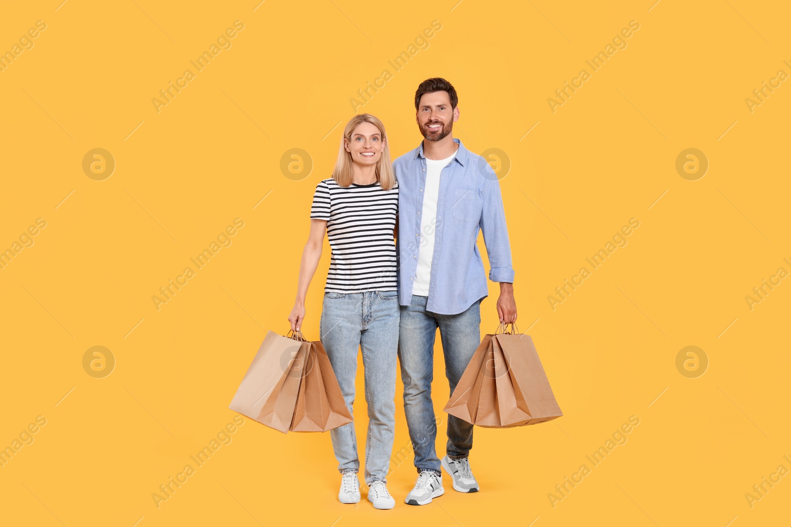 Photo of Family shopping. Happy couple with paper bags on orange background