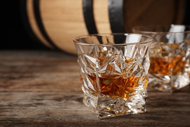 Photo of Golden whiskey in glass with ice cubes on wooden table. Space for text