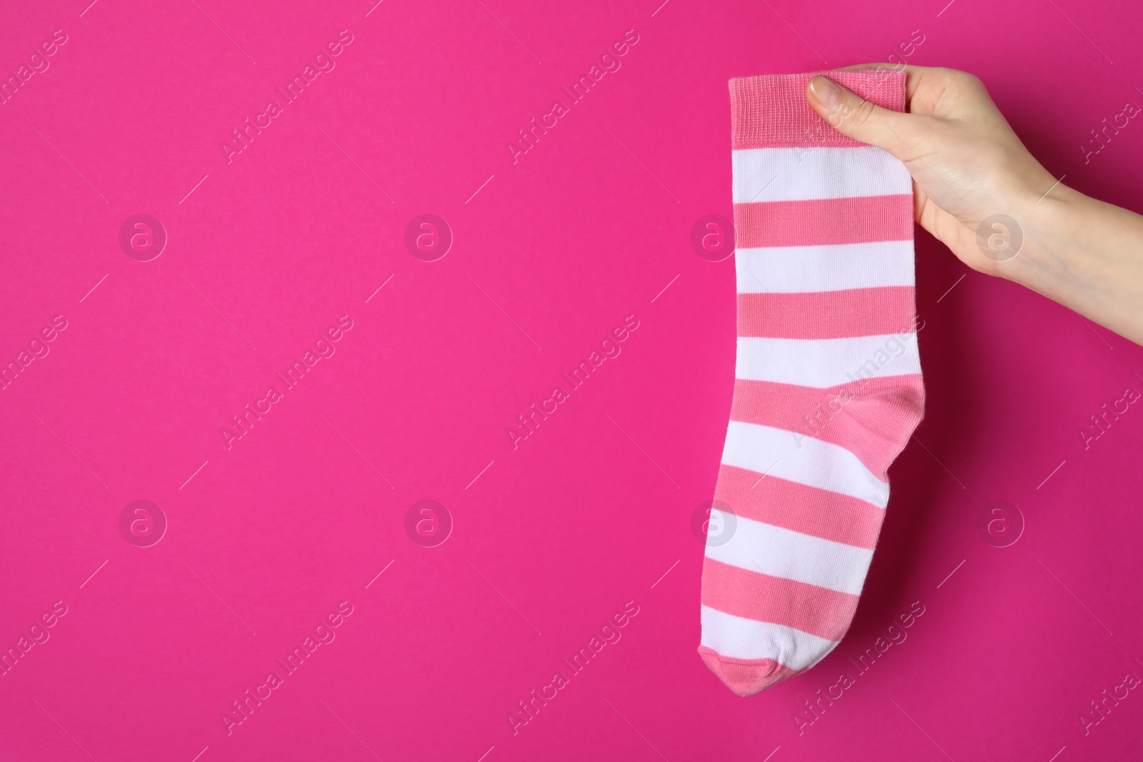 Photo of Woman holding striped sock on bright pink background, closeup. Space for text