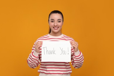 Photo of Happy woman holding card with phrase Thank You on orange background