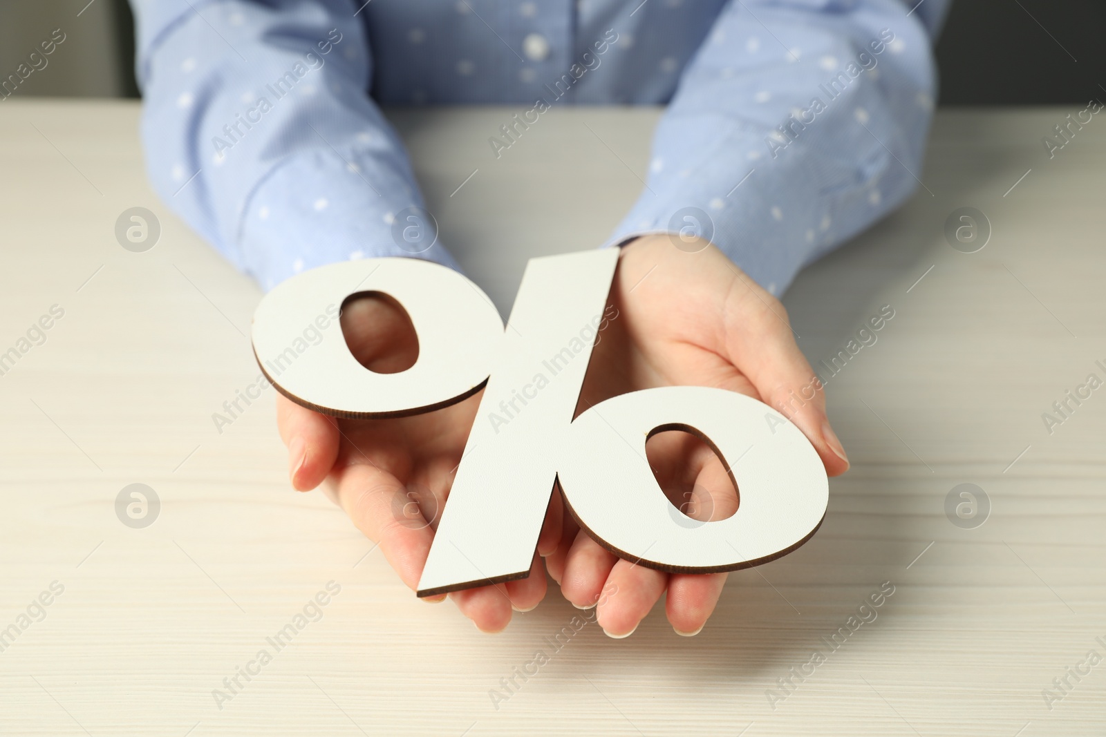 Photo of Woman holding percent sign at white wooden table, closeup