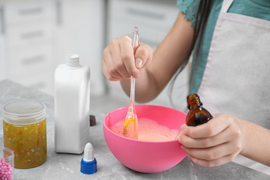 Little girl mixing ingredients with silicone spatula at table indoors, closeup. DIY slime toy