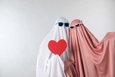 Cute ghosts. Couple in color sheets and sunglasses with red heart on light grey background, space for text