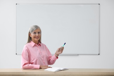 Professor with marker giving lecture at desk in classroom, space for text