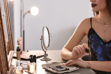 Photo of Young woman applying makeup indoors