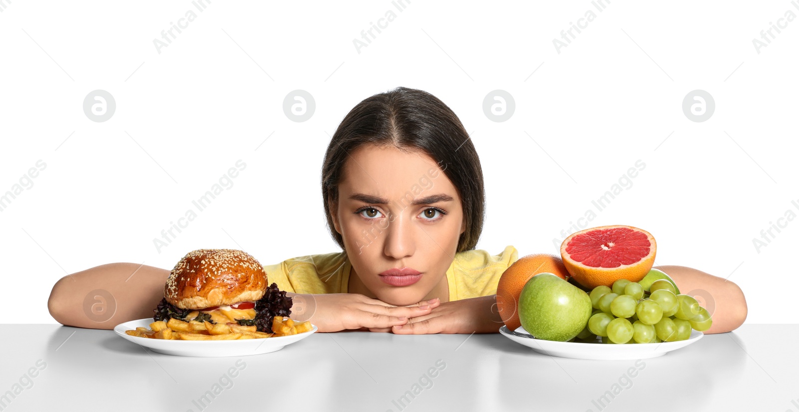 Photo of Woman choosing between fruits and burger with French fries on white background