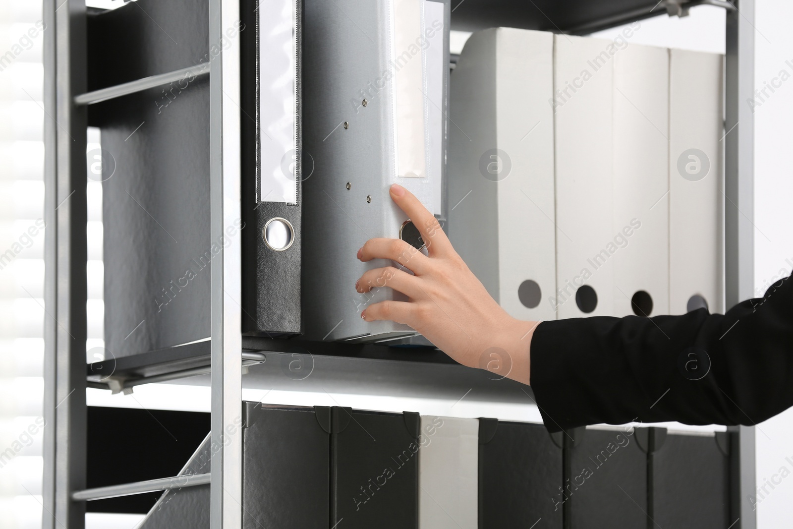 Photo of Woman taking folder with documents from shelf in office, closeup