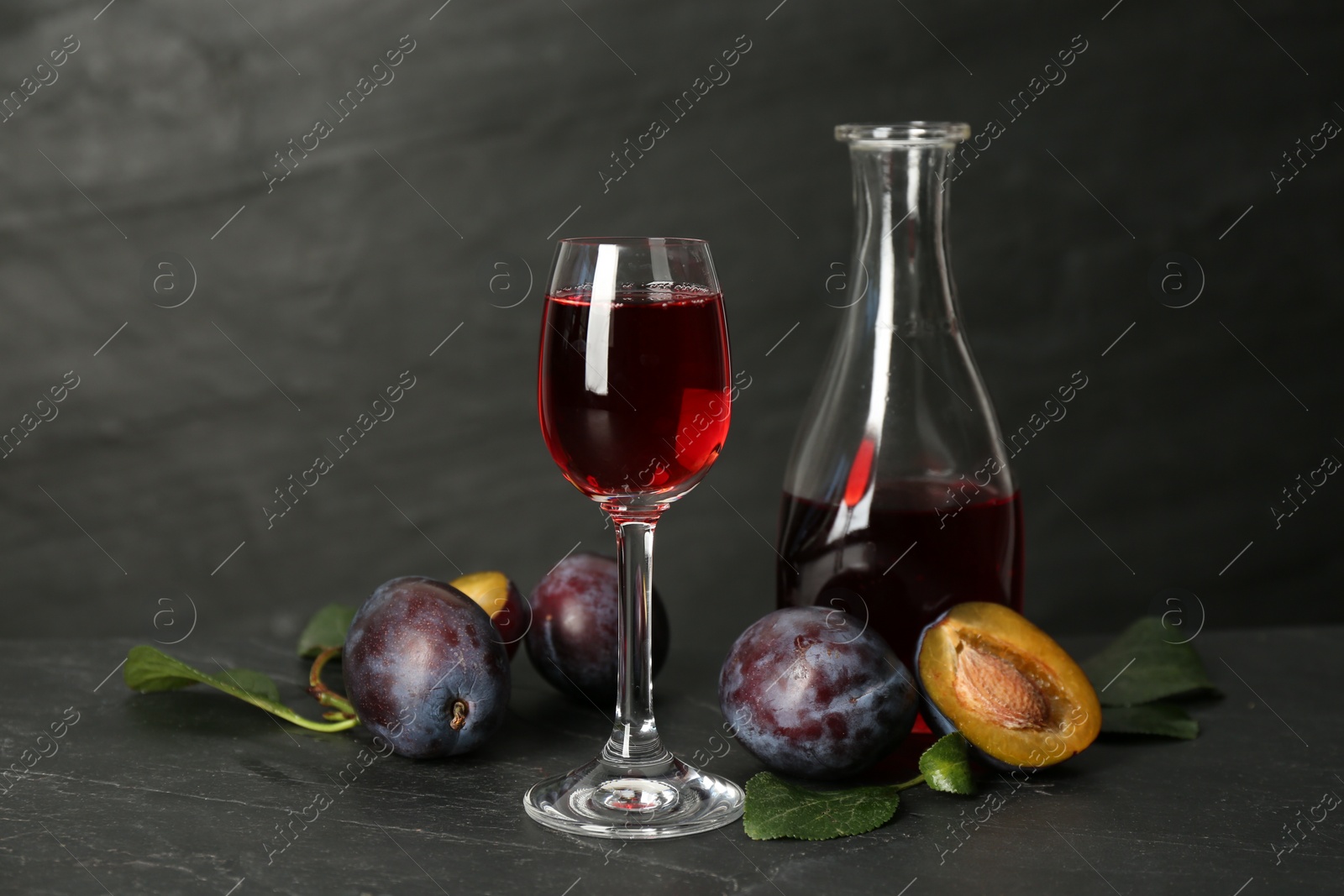 Photo of Delicious plum liquor and ripe fruits on black table. Homemade strong alcoholic beverage