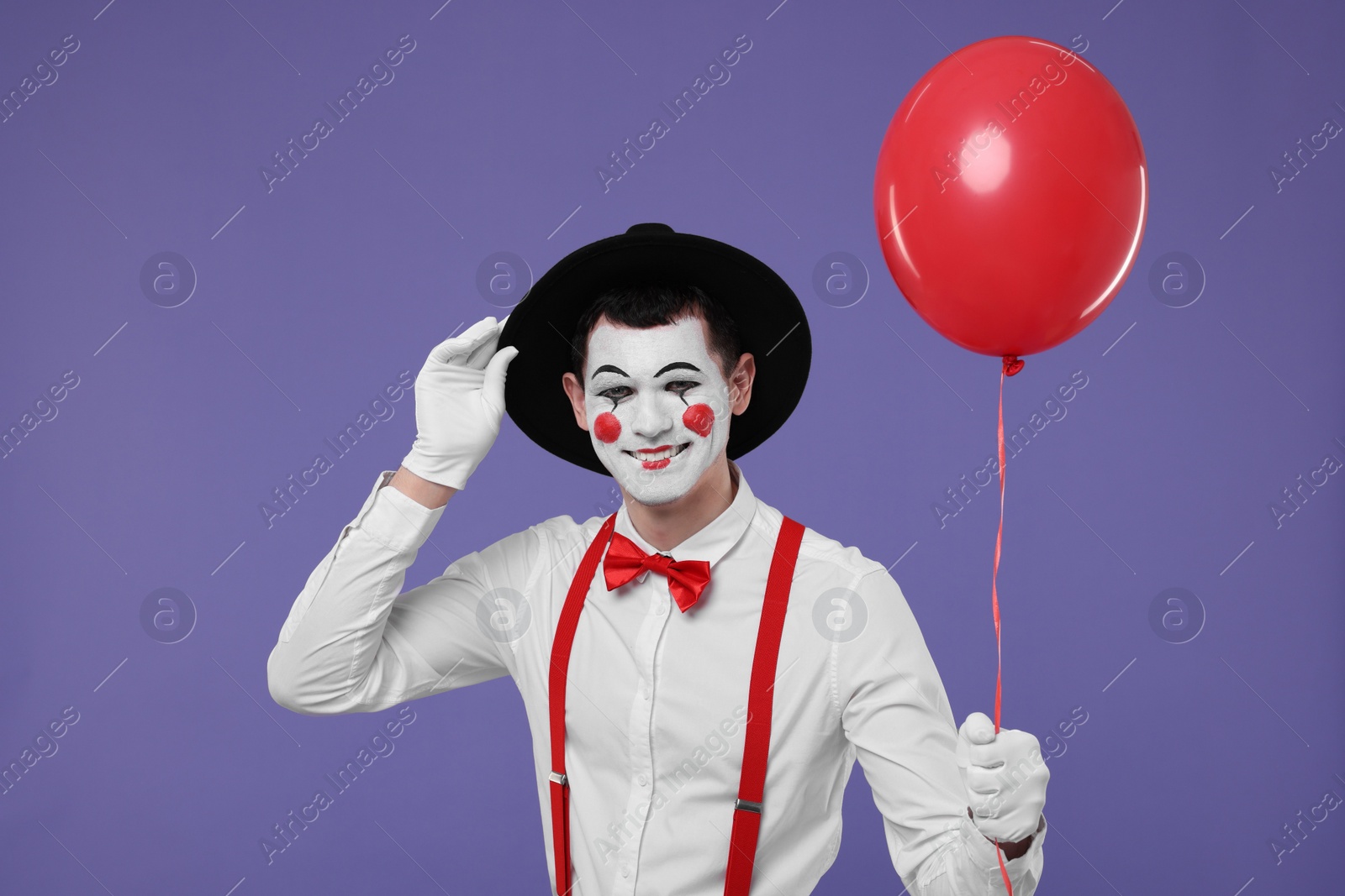 Photo of Funny mime artist with red balloon on purple background