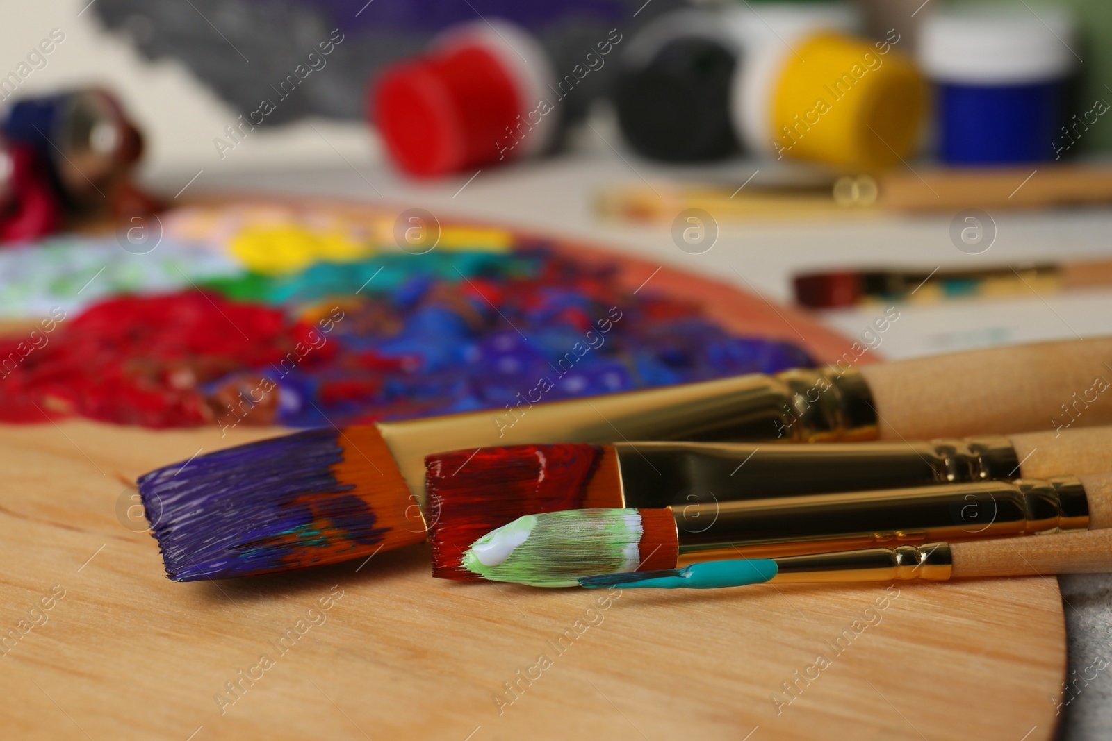 Photo of Artist's palette with mixed paints and brushes on table, closeup