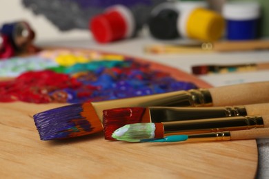 Photo of Artist's palette with mixed paints and brushes on table, closeup