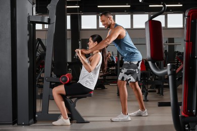 Photo of Happy trainer showing woman how to do exercise properly in modern gym