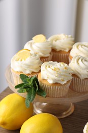 Photo of Delicious lemon cupcakes with white cream, mint and lemons on table, closeup