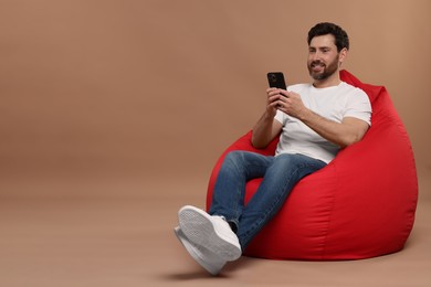 Photo of Smiling man with smartphone sitting on bean bag against light brown background. Space for text