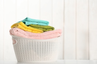 Basket with clean laundry on table against light background, space for text