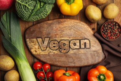 Board with word Vegan and fresh vegetables on wooden background, flat lay