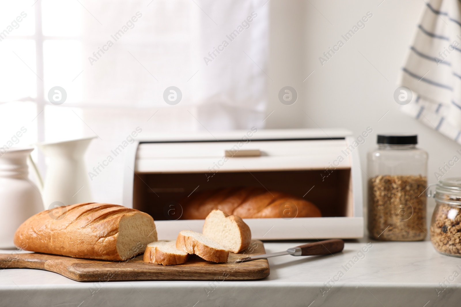 Photo of Wooden bread basket with freshly baked loaves on white marble table in kitchen