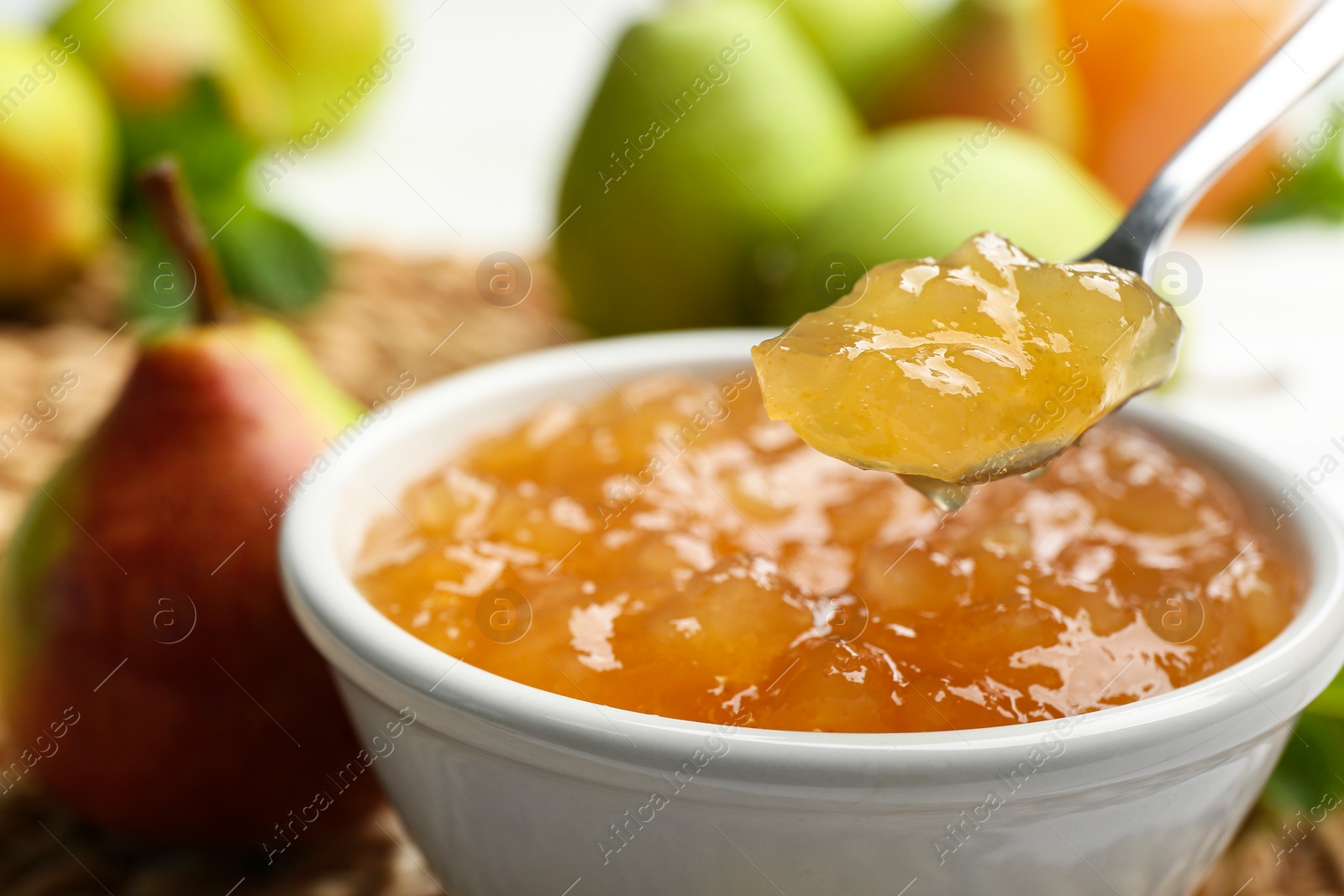 Photo of Spoon with delicious pear jam over bowl, closeup