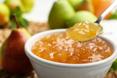 Spoon with delicious pear jam over bowl, closeup