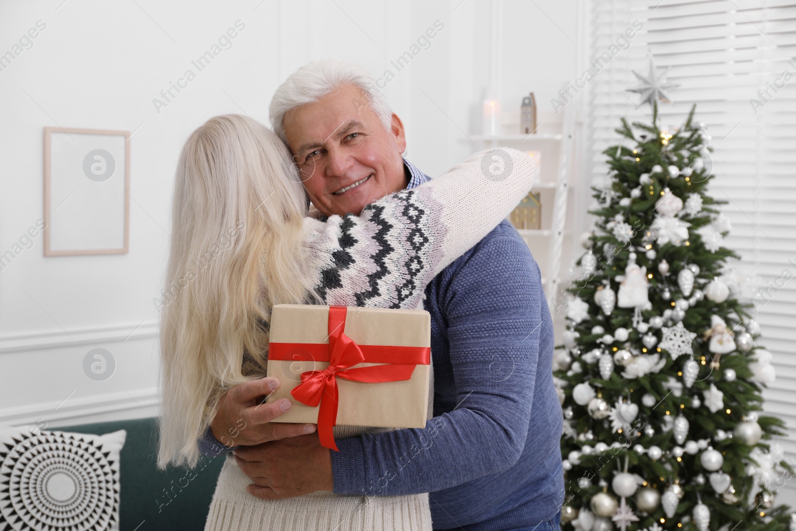 Photo of Happy mature couple with gift box hugging at home. Christmas celebration