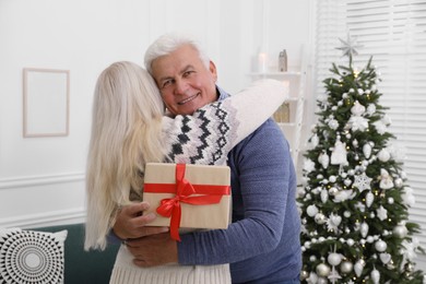 Photo of Happy mature couple with gift box hugging at home. Christmas celebration