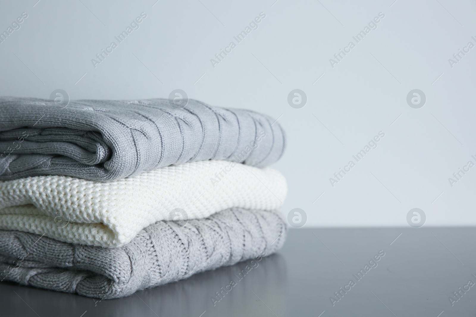 Photo of Stack of folded knitted sweaters on grey table. Space for text